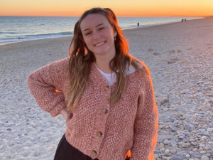 une fille d'une vingtaine d'année qui sourit en posant devant la plage