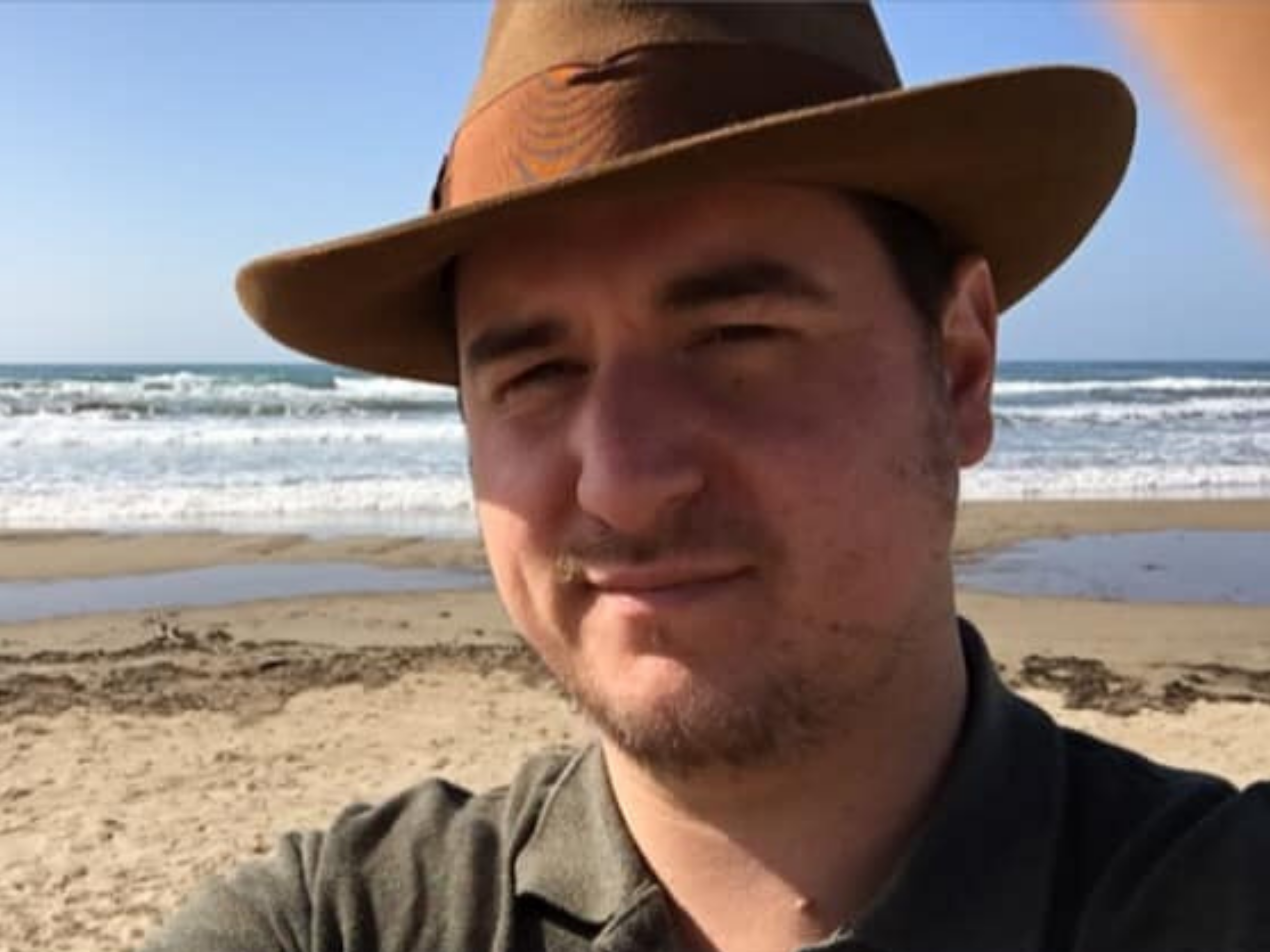 Un homme devant la mer qui a un chapeau de cowboy sur la tête